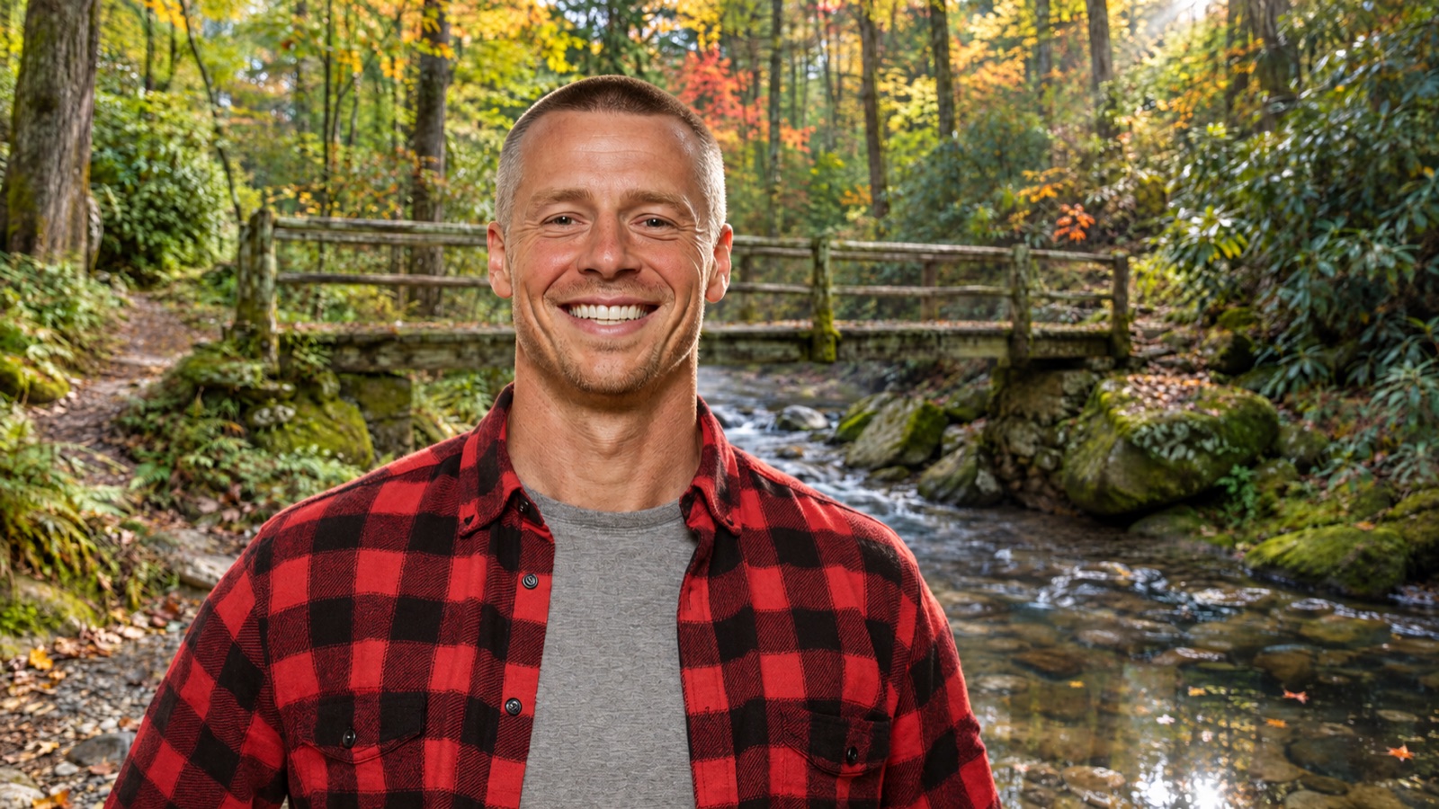 Dust Akerson smiling in a red flannel shirt beside a creek and footbridge in autumn
